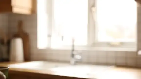 A hand holding a small glass of pale green liquid up to a kitchen window and swirling it once