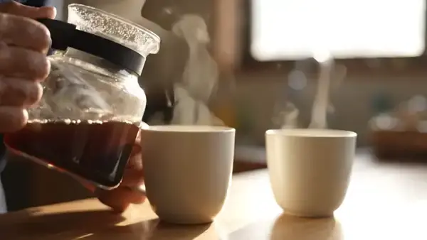 Brewed coffee poured into a white mug and then split into a second smaller cup by a man's hands