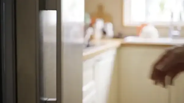 A hand taking one small green bottle from a row in a refrigerator door rack